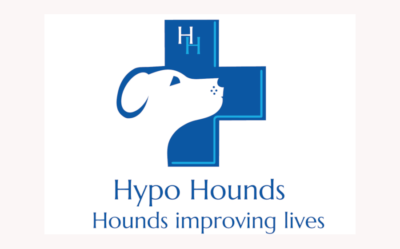 Hypo Hounds Logo: the outline of a dog face transposed over a blue cross with the words Hounds Improving Lives
